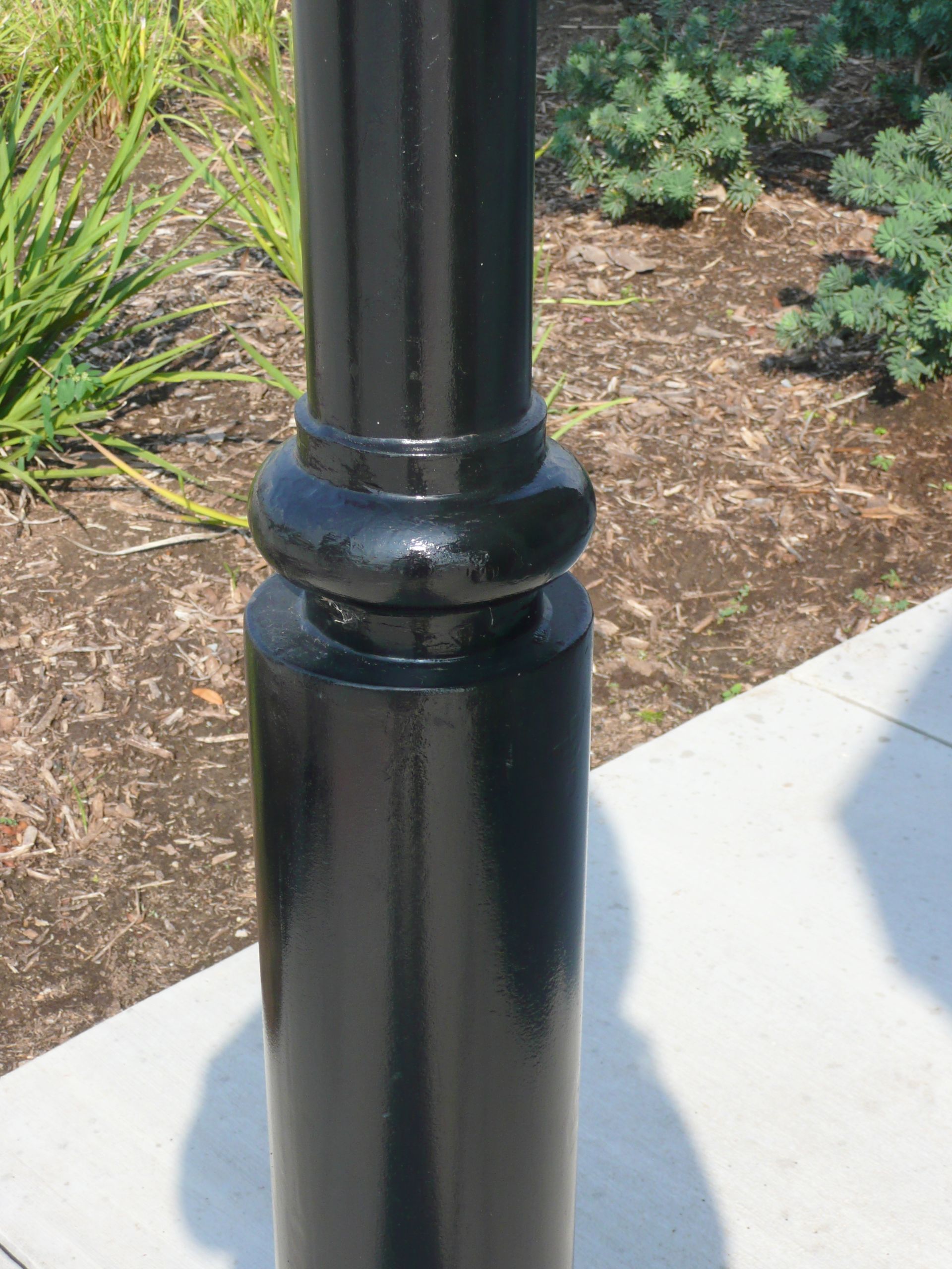 A black pole is sitting on a sidewalk next to a garden.