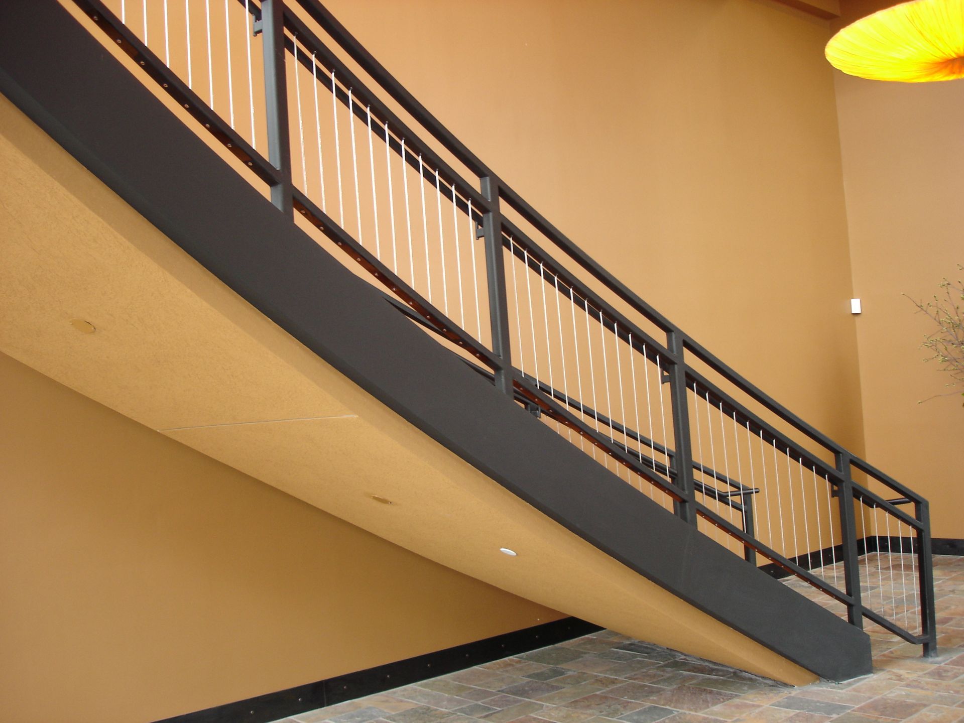 A staircase with a black railing and a yellow light hanging from the ceiling