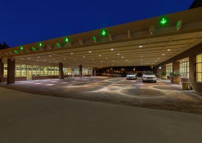 A parking lot with cars parked under a canopy at night.