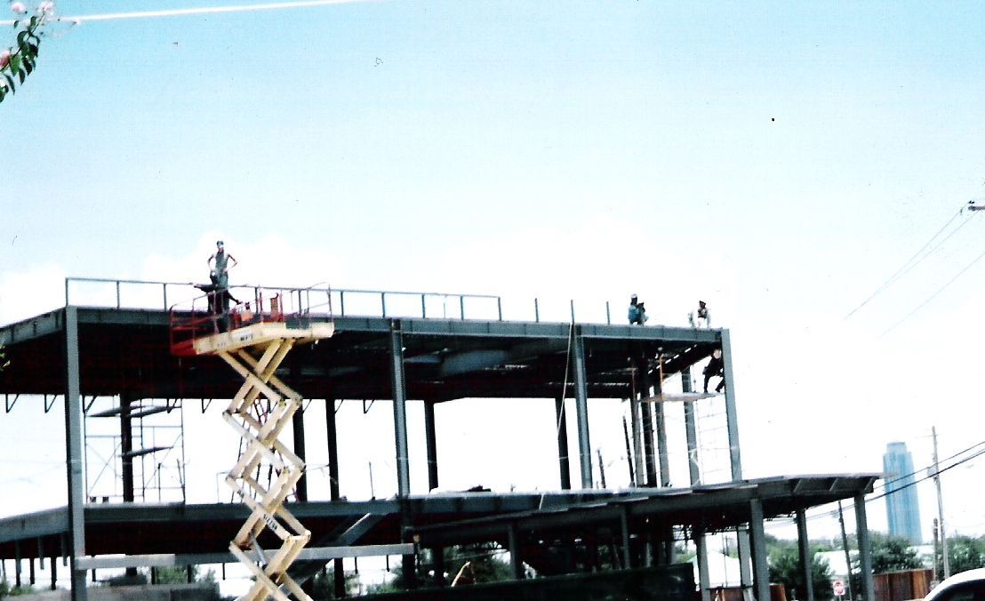 A large building under construction with a scissor lift in the foreground.