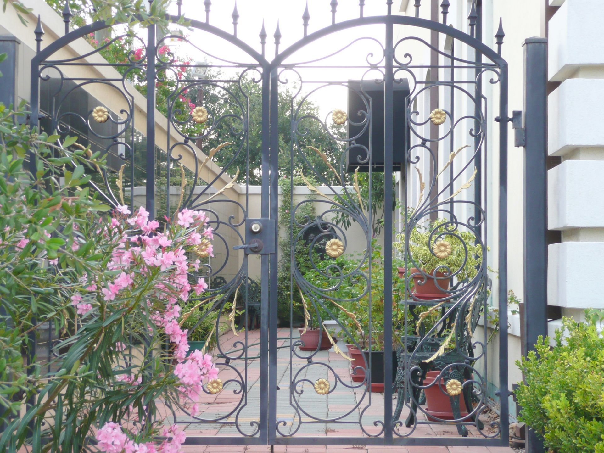 A wrought iron gate with pink flowers in front of it