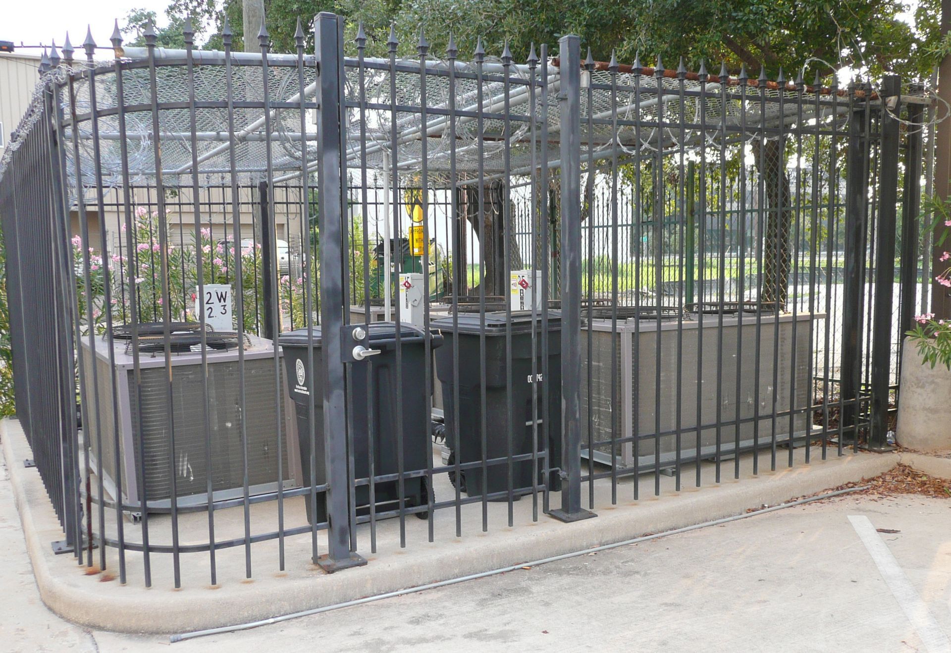 A wrought iron fence surrounds a building with air conditioners behind it