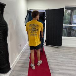 Man in yellow shirt, moving object on red carpet indoors.