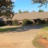 Brown brick house with light brown driveway and green grass under a blue sky.