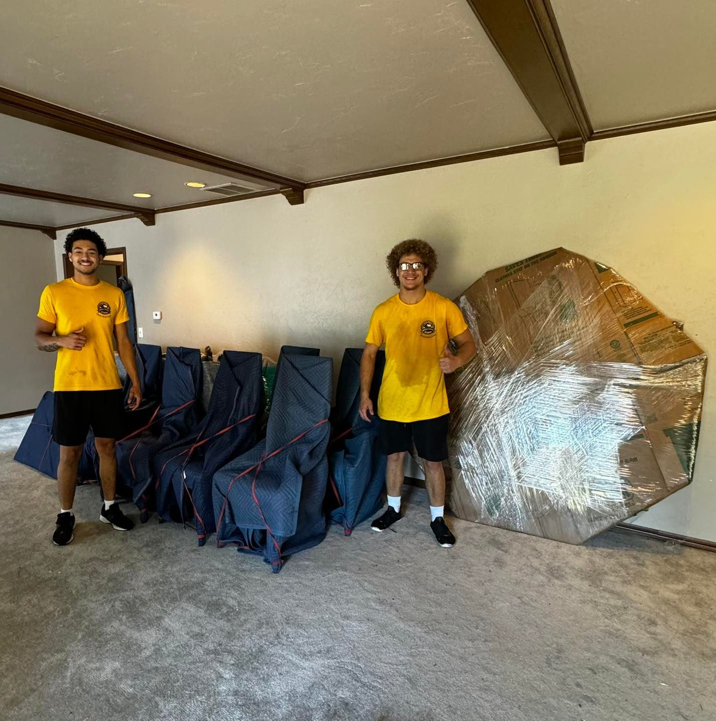Two people pose with furniture wrapped for moving.