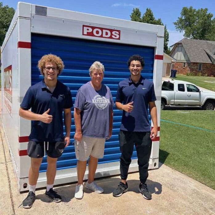 Three people stand in front of a blue PODS container. They give thumbs-up gestures on a sunny day.