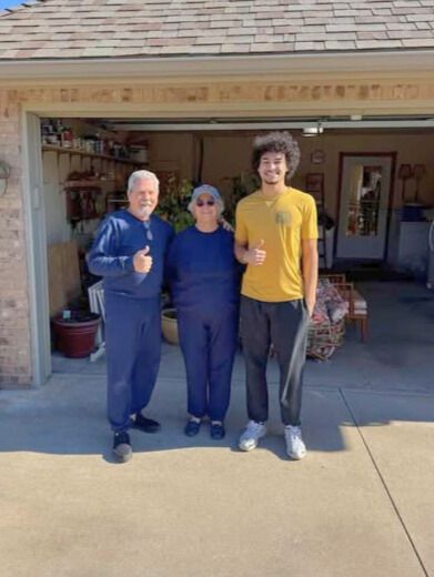 Three people stand outside a garage, giving thumbs up.