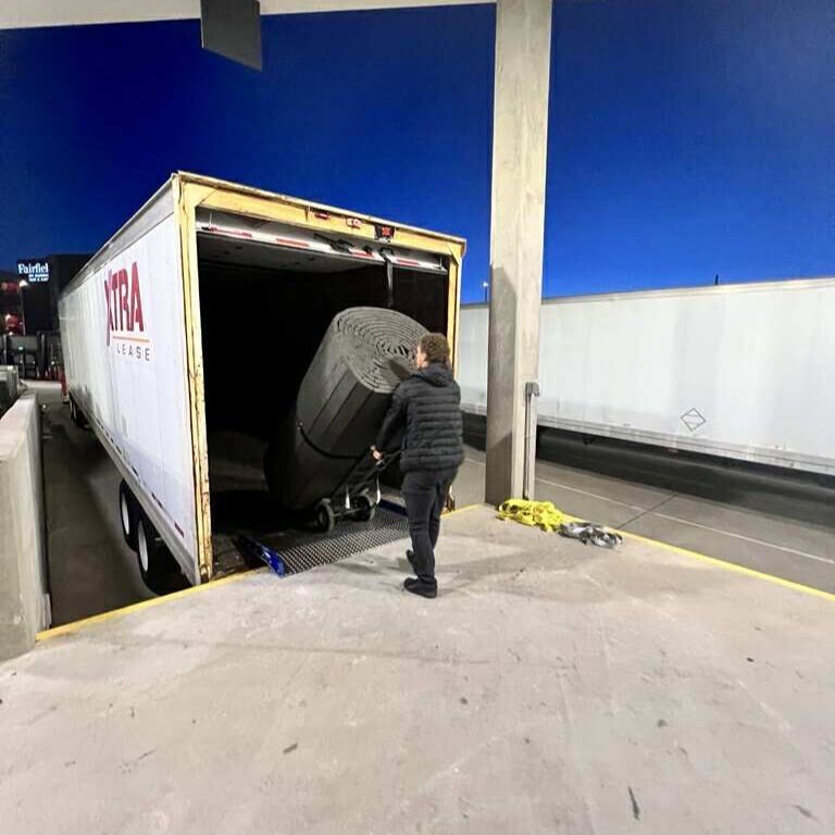 A person loads a large, rolled object into a truck trailer at a loading dock at night.