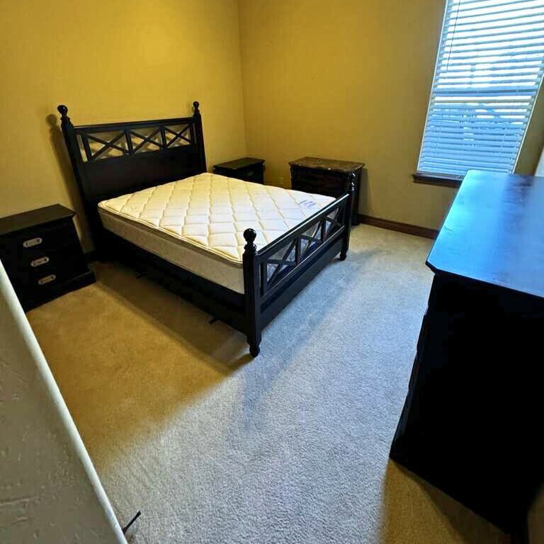 Bedroom with a black bed frame, mattress, two nightstands, a dresser, and a window with blinds.