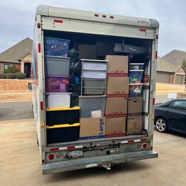 Back of a moving truck packed with boxes and bins on a residential driveway.