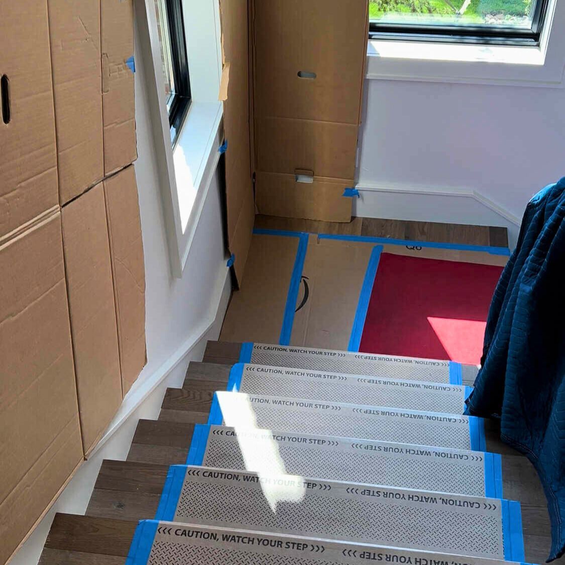 Staircase protected by cardboard and tape, leading up, next to a window.