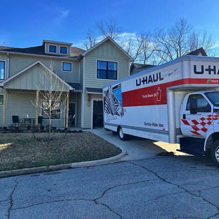 U-Haul truck parked in front of a light green house, possibly moving. Sunny day, clear blue sky.