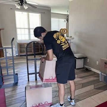 Person unpacking boxes in a living room; a hand truck and boxes are nearby.