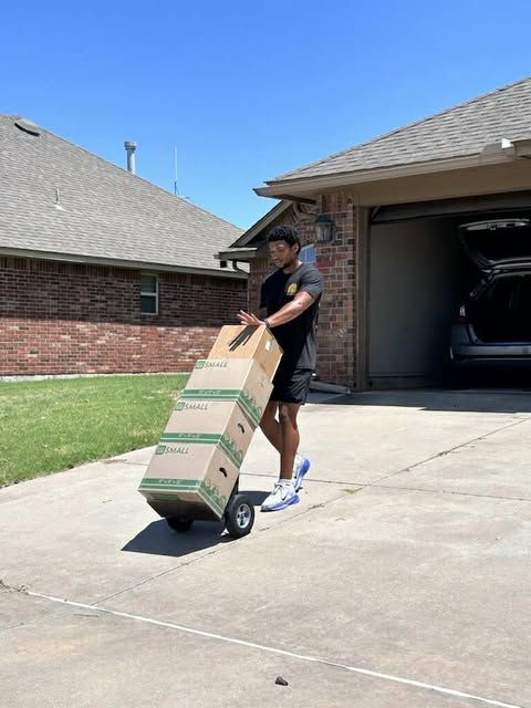 Person pulling a tall box on a dolly out of a garage on a sunny day.