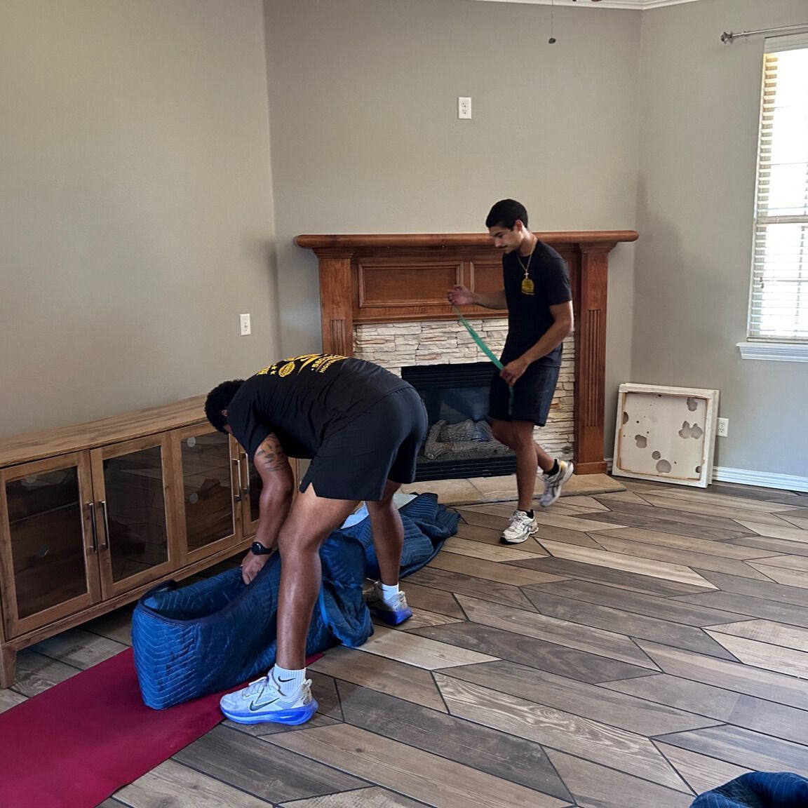 Man in yellow shirt and shorts stands by a large wooden cabinet in front of patterned wallpaper.