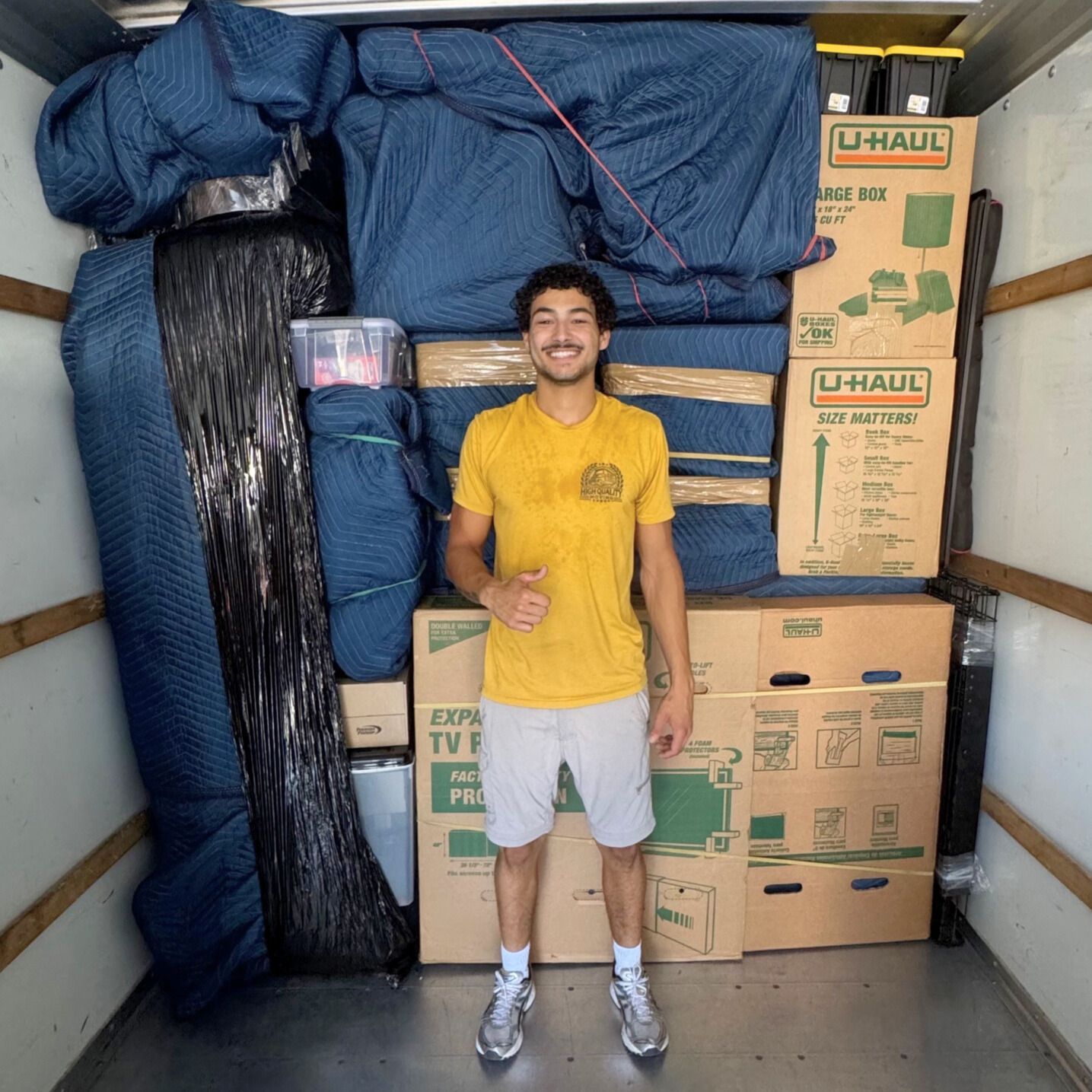 Man in a yellow shirt standing in a packed moving truck, giving a thumbs-up.