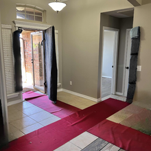 Red carpet covers flooring inside a home.  Doorways are draped with padded protection, and a door is open.