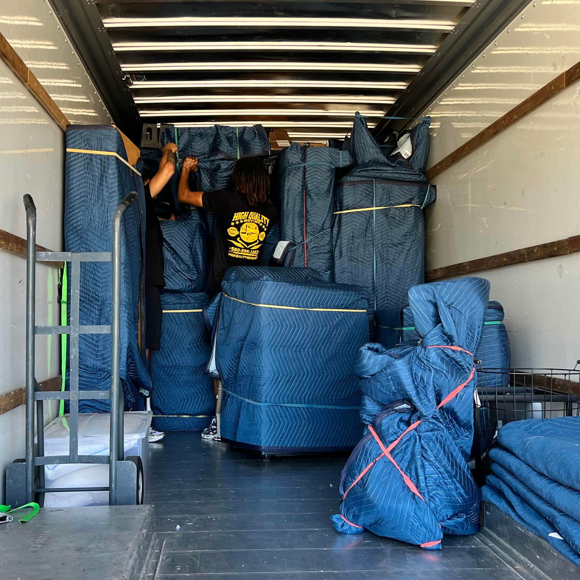 Inside a moving truck, movers loading furniture wrapped in blue pads.