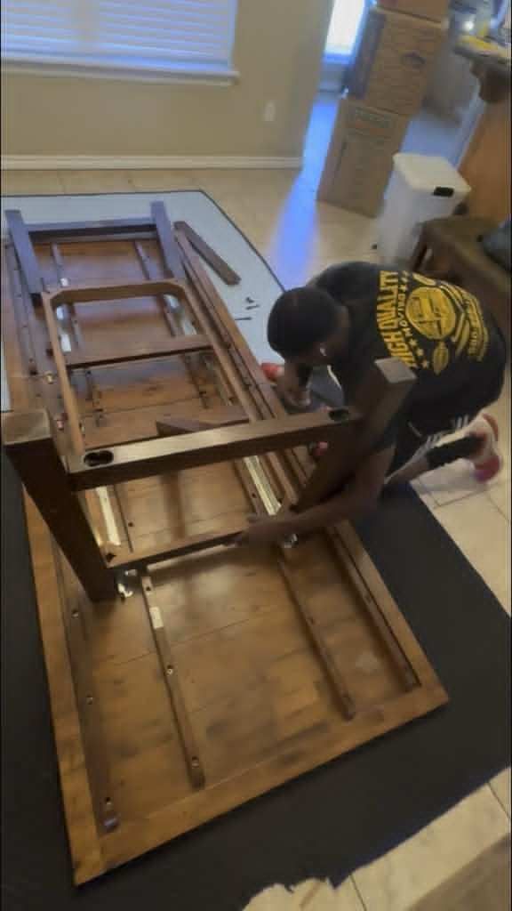 Person assembling a wooden dining table on a floor mat indoors.