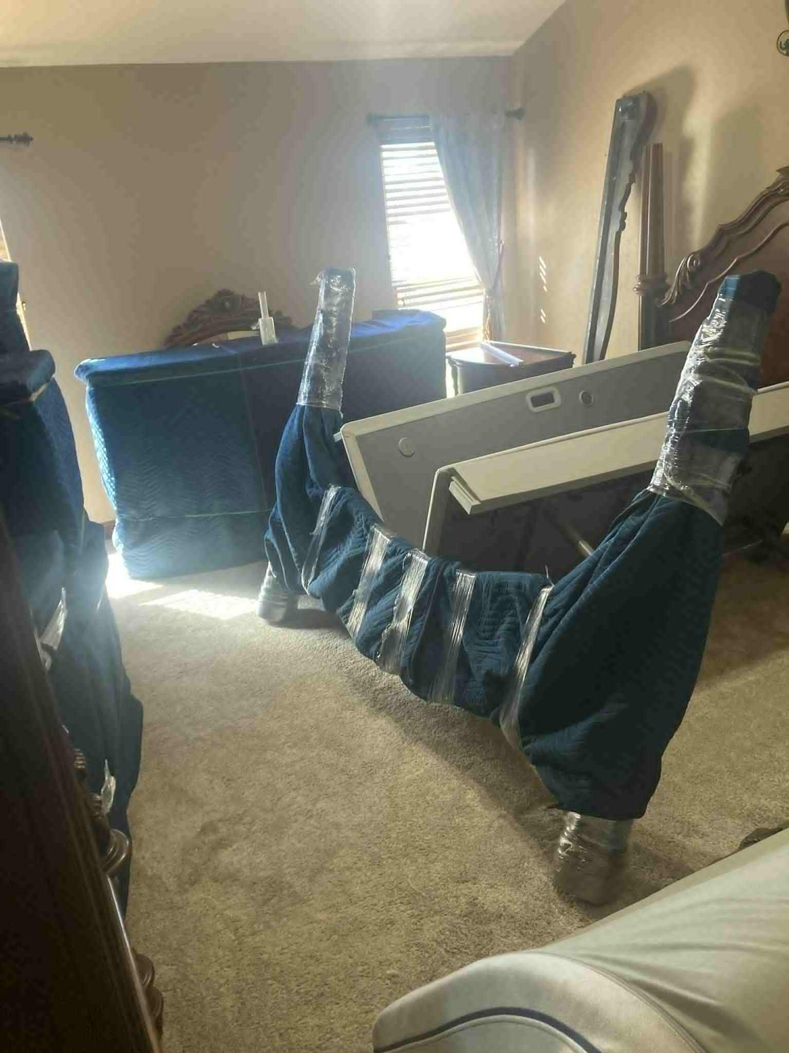Blue fabric-wrapped bed frame supported by silver-taped legs in a room with furniture.