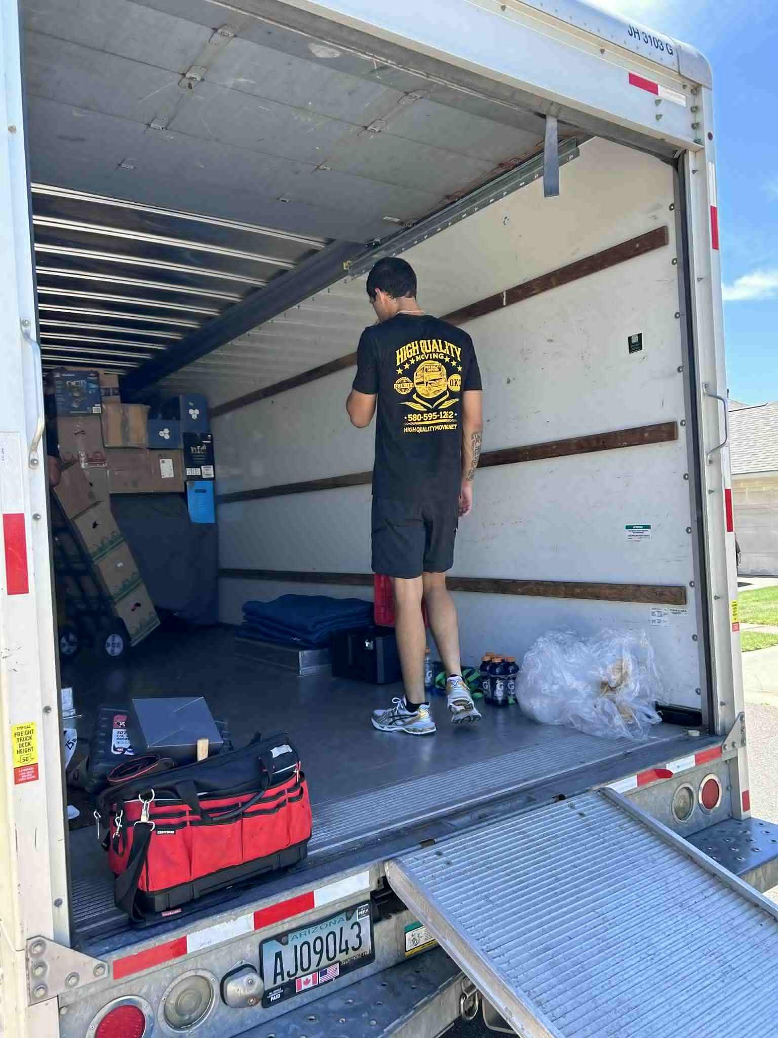 Man inside a moving truck. He is wearing shorts and a t-shirt. Boxes and belongings are inside.