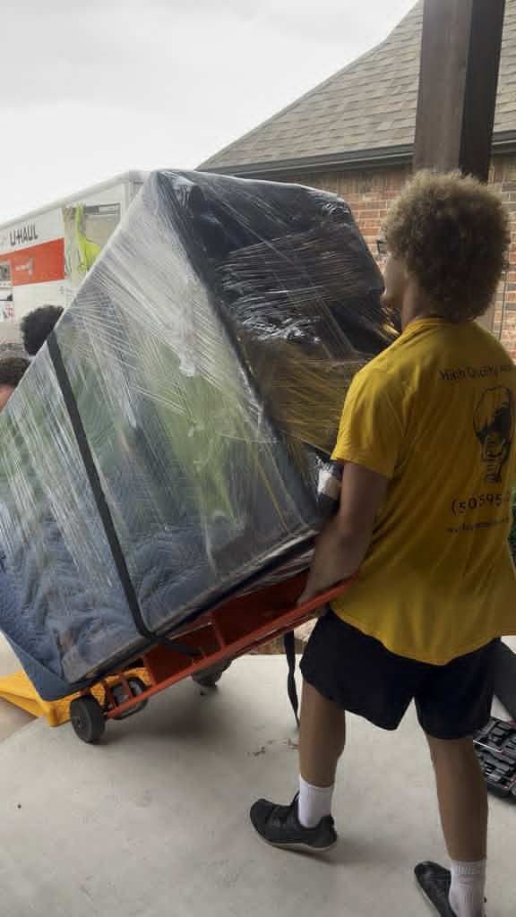 mover pushing a wrapped gun safe on a dolly toward a moving truck.