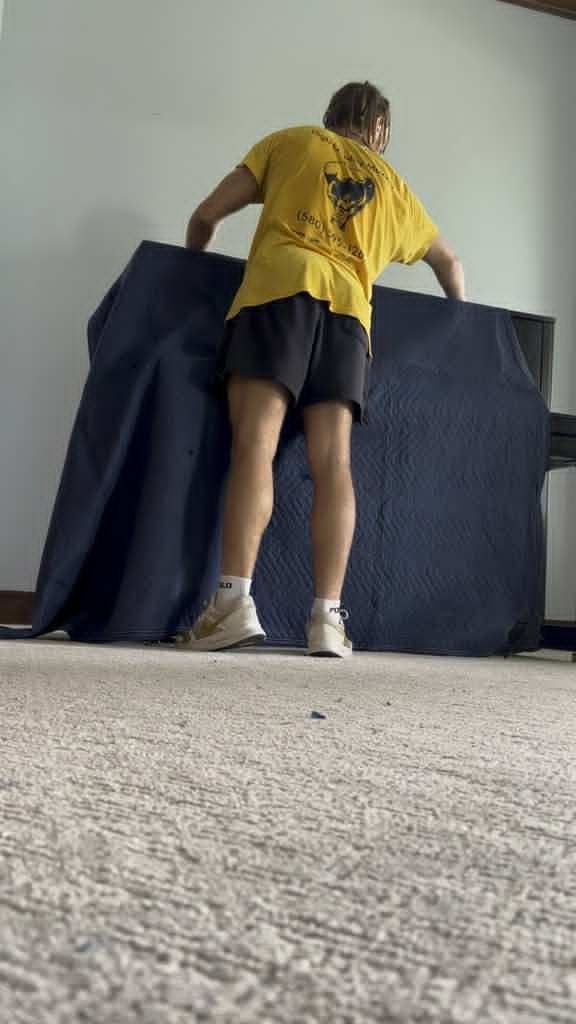 Person lifting a covered piano against a wall on carpet.