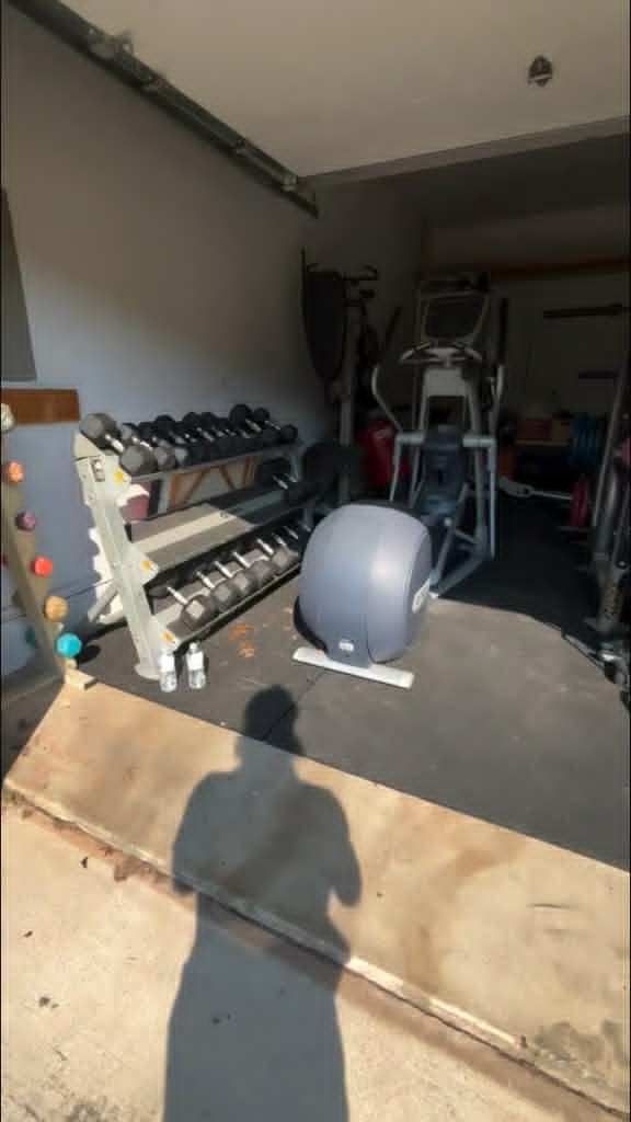 Home gym with dumbbell rack, exercise ball, and various equipment. Shadow of person in the foreground.