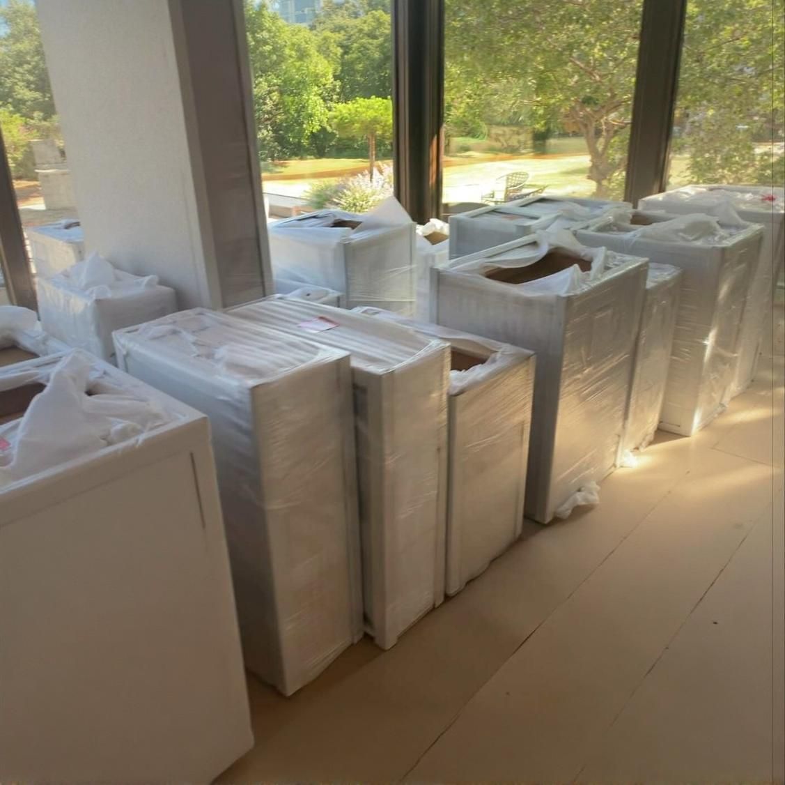 Boxes wrapped in plastic, lined up in a room with a window, ready for moving.