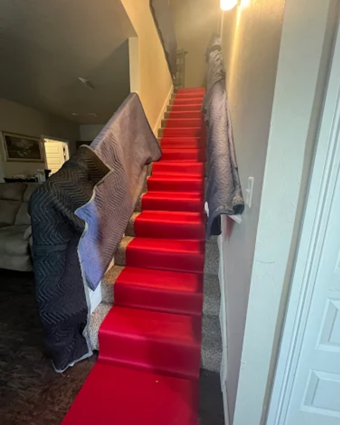 Red carpet runner on a staircase, protected by moving blankets. Beige walls.