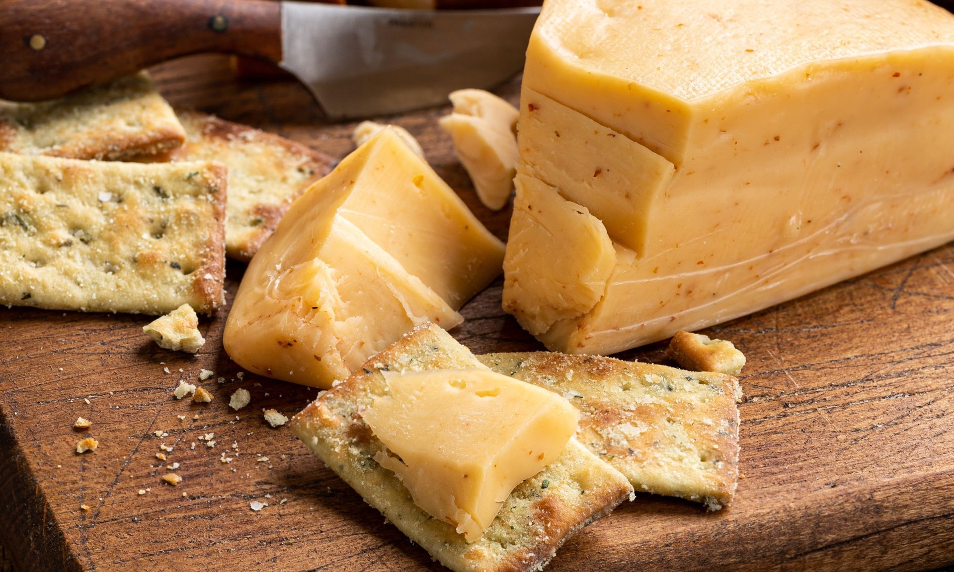 Een stuk kaas ligt op een houten snijplank naast crackers.