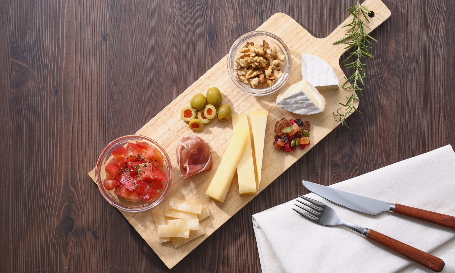 Een houten snijplank gevuld met kaas, olijven, tomaten en ham.