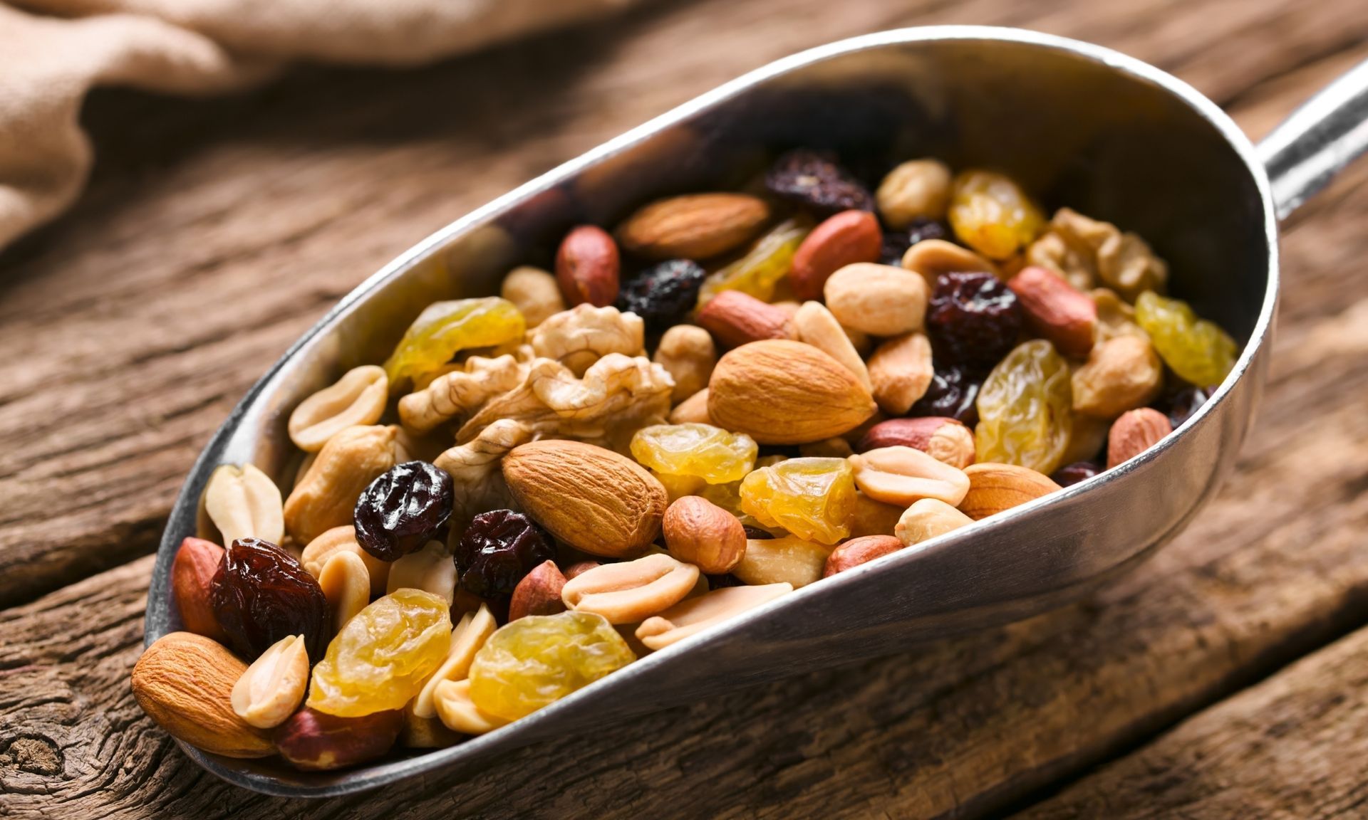 Een metalen lepel gevuld met noten en rozijnen op een houten tafel.