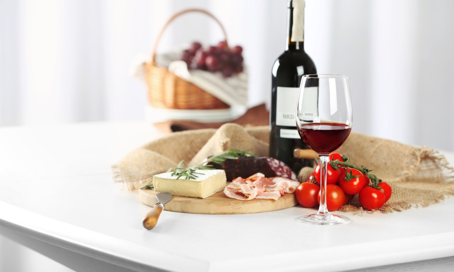 Een fles wijn, een glas wijn, tomaten, kaas en ham staan op tafel.