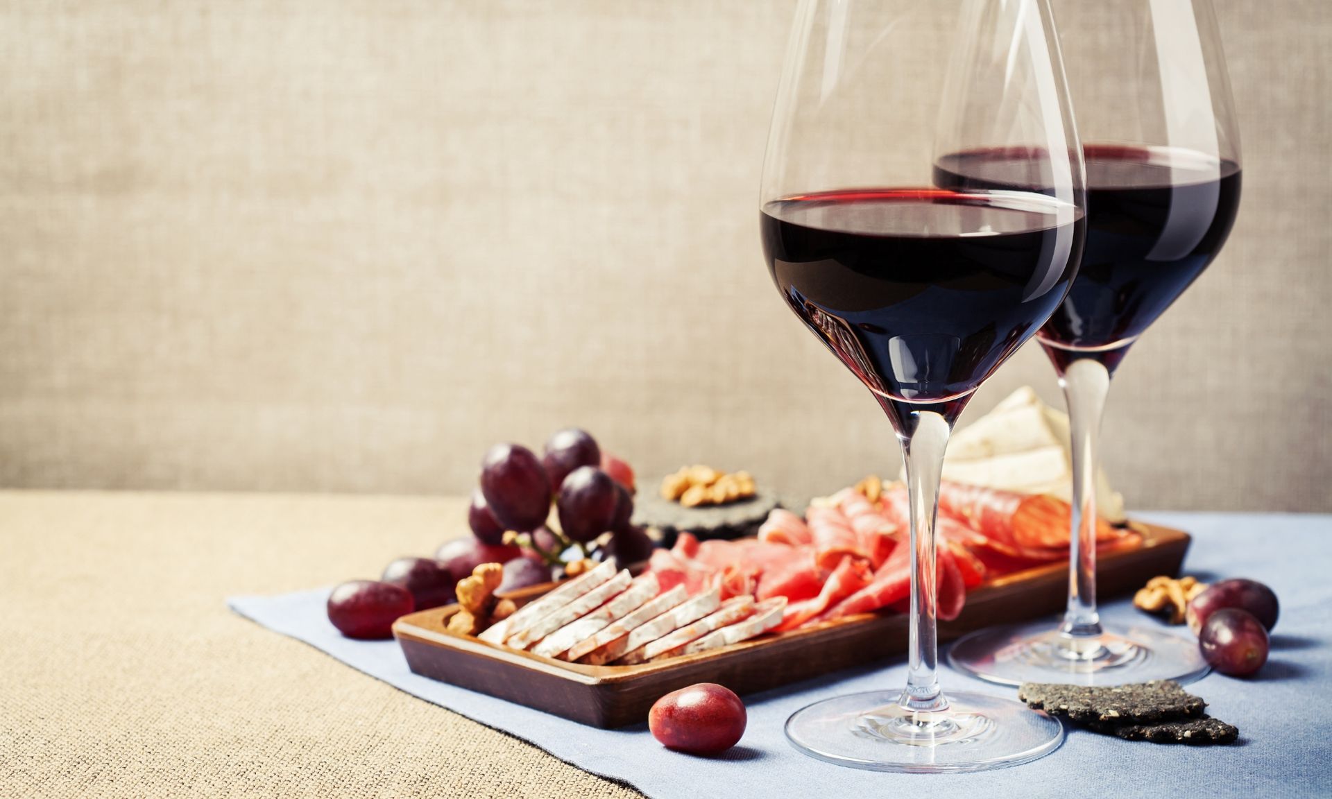 Twee glazen rode wijn staan op een tafel, naast een snijplank met vlees en druiven.