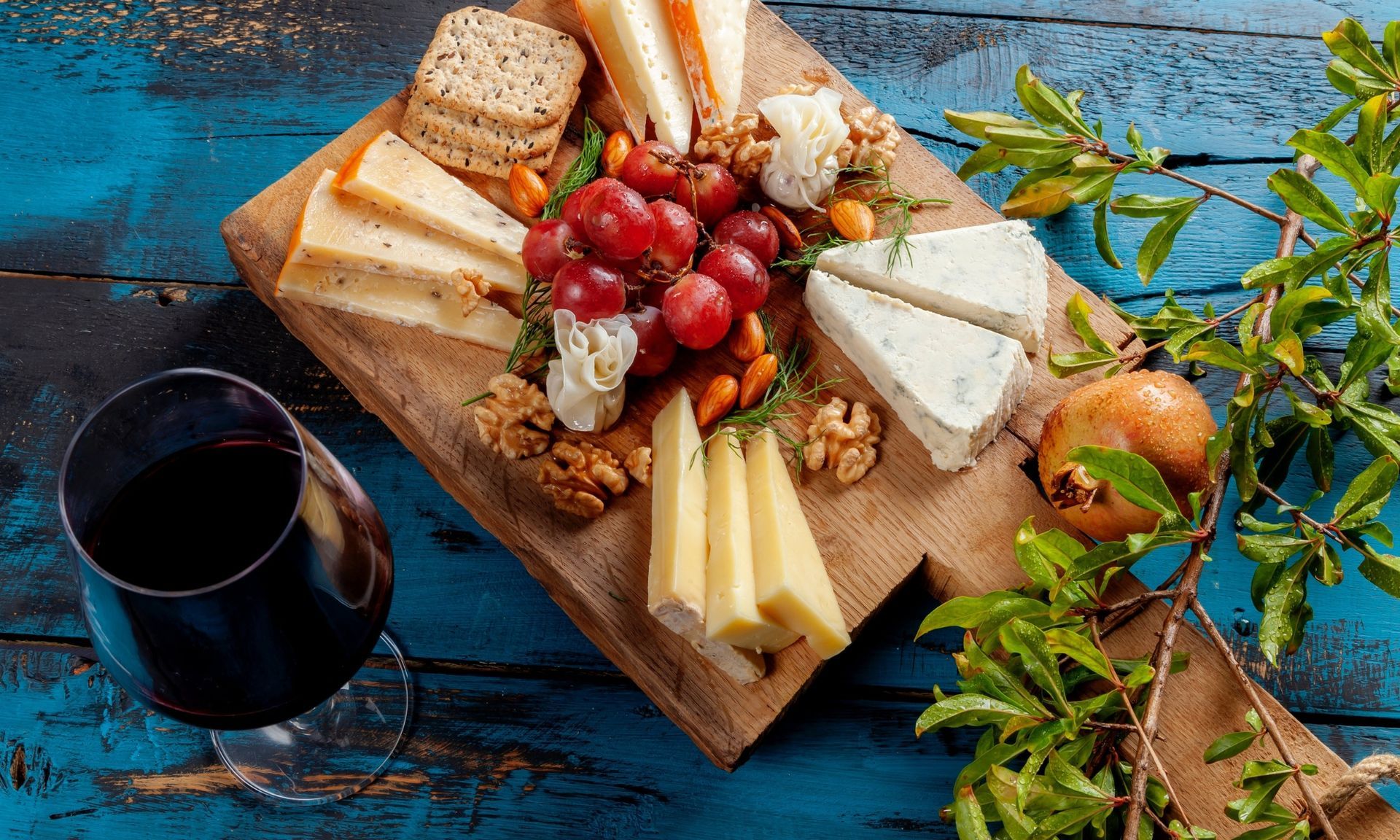 Een houten snijplank met kaas, druiven, noten en een glas wijn.