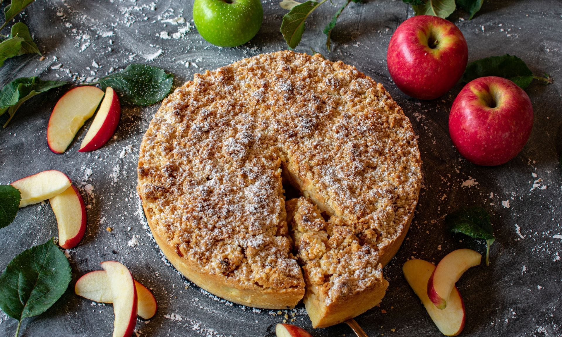 Een taart waar een punt uit is gehaald, omgeven door appels en bladeren.