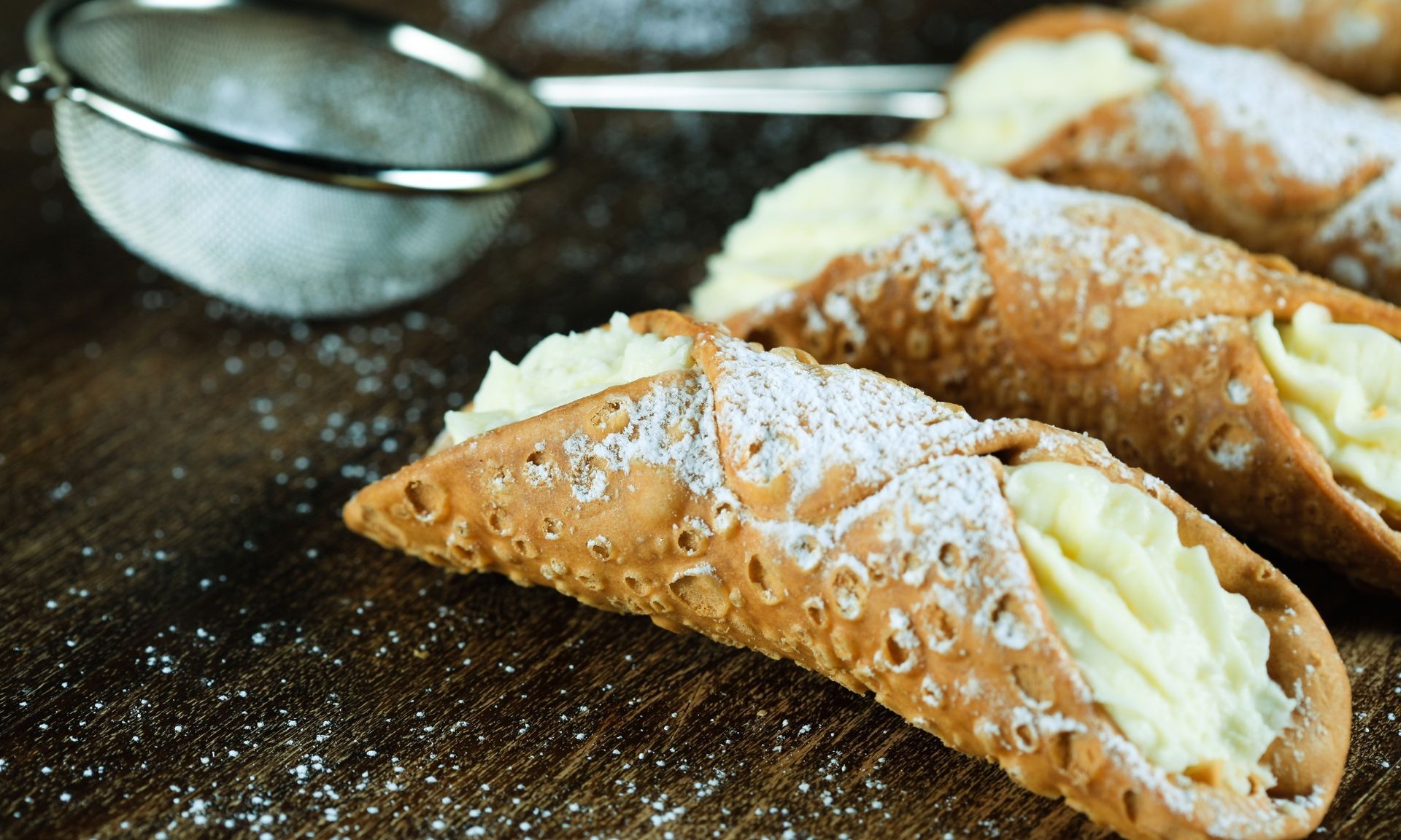 Een close-up van een cannoli met poedersuiker op een houten tafel.