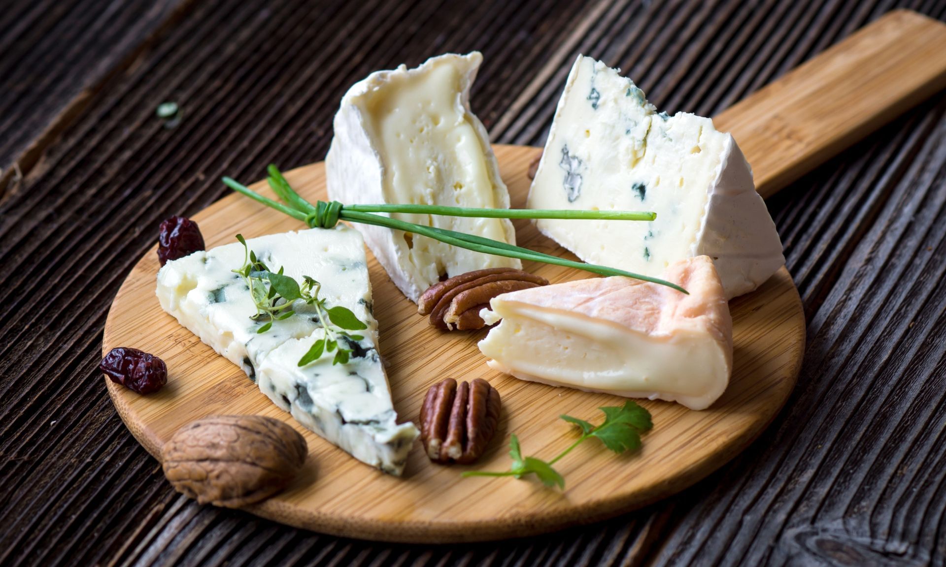 Een houten snijplank belegd met verschillende soorten kaas en noten.