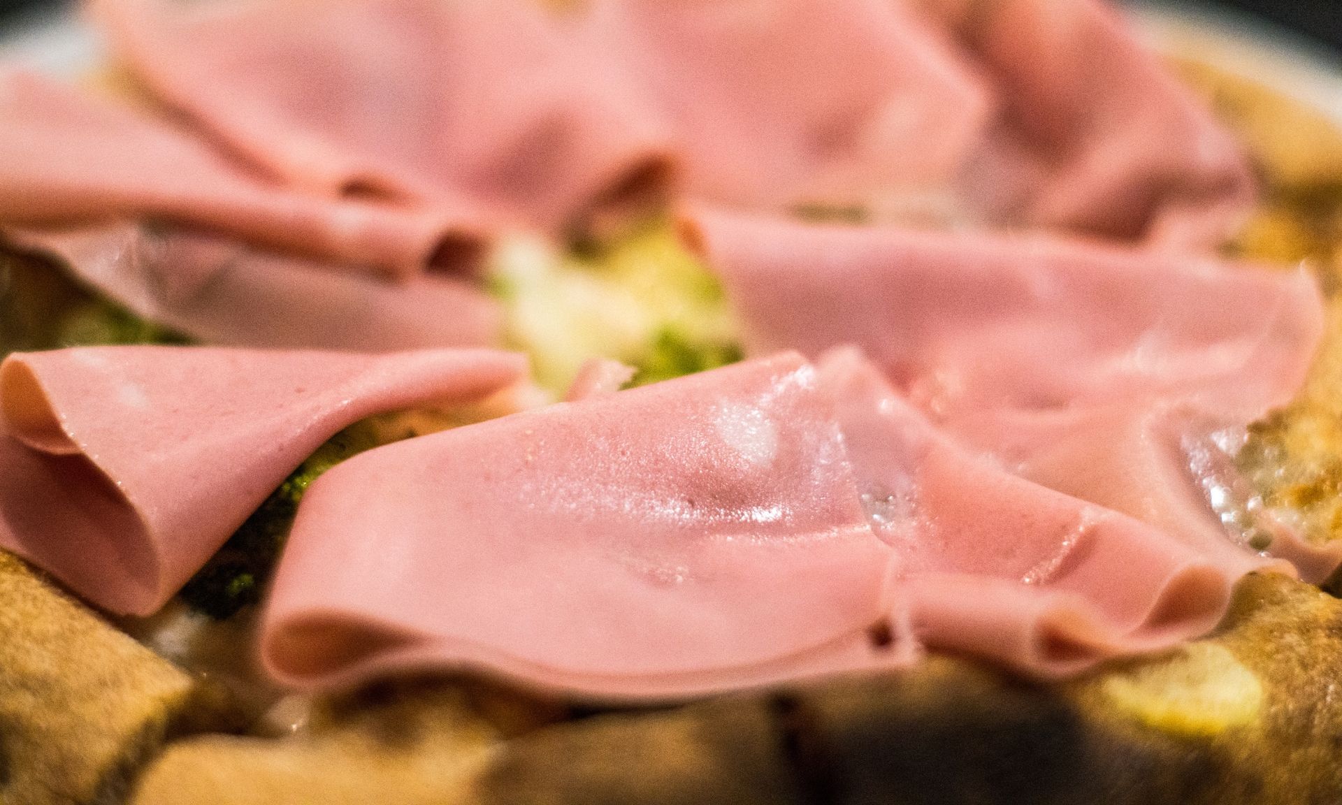 Een close-up van een pizza met ham en broccoli op een bord.