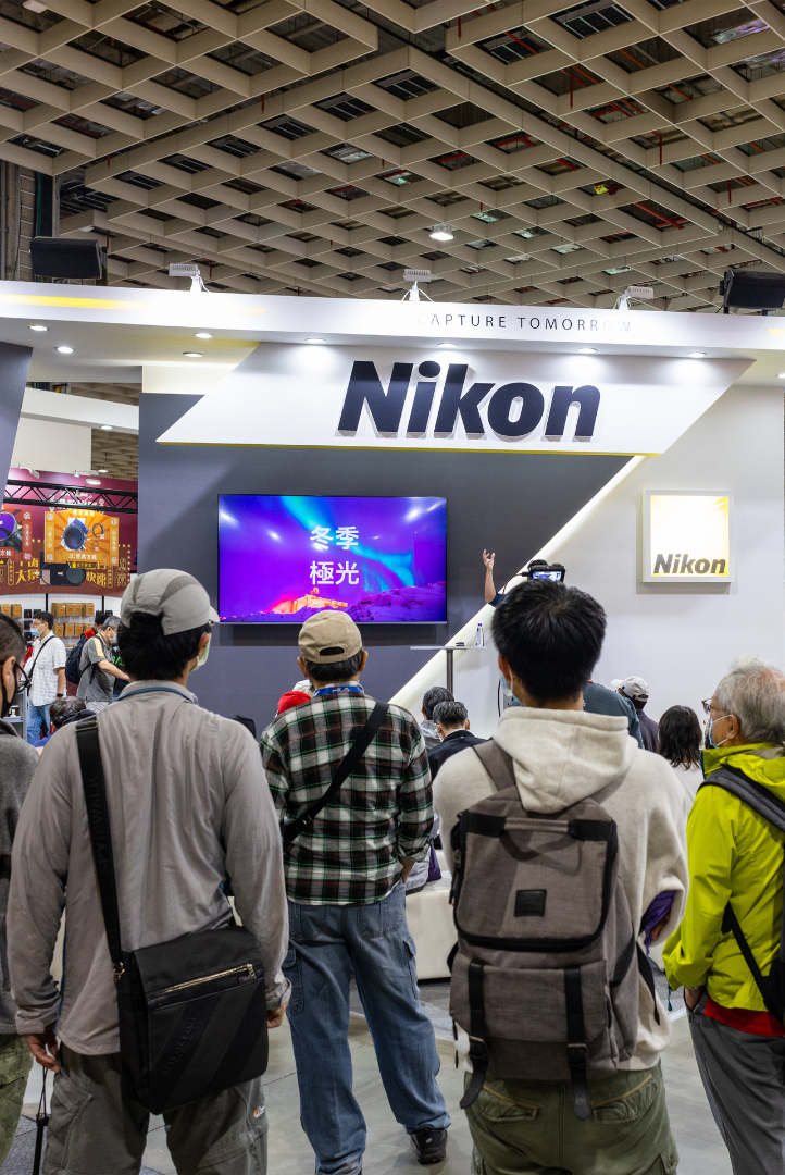 A group of people are standing in front of a nikon booth at a convention.