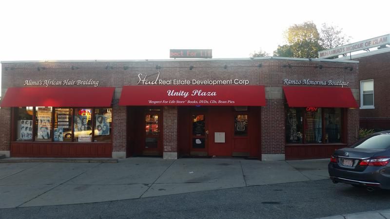 A car is parked in front of a brick building with red awnings.