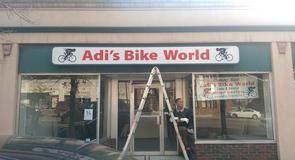 A man is standing in front of a store called adi 's bike world.