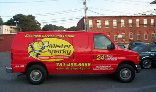 A red mister sparky van is parked in front of a building
