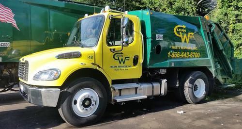 A yellow and green garbage truck is parked in a parking lot.