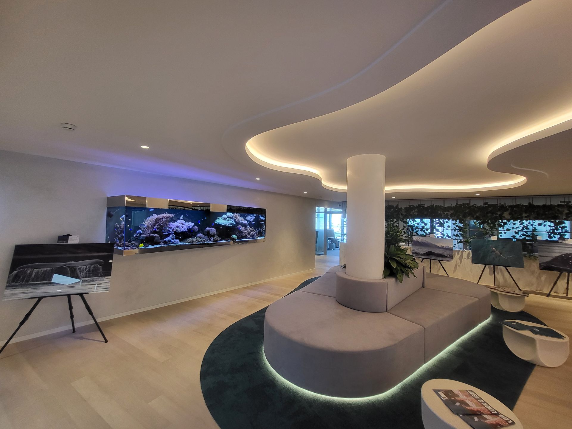 Espace lounge moderne avec un long aquarium, des sièges incurvés et un plafond décoratif.