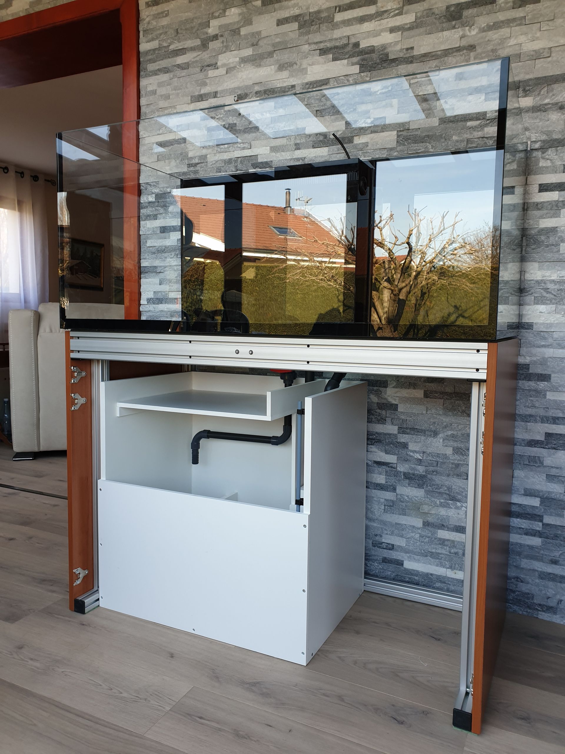 Un aquarium moderne composé de trois aquariums en verre reliés entre eux, d'un meuble blanc et d'un cadre en bois.