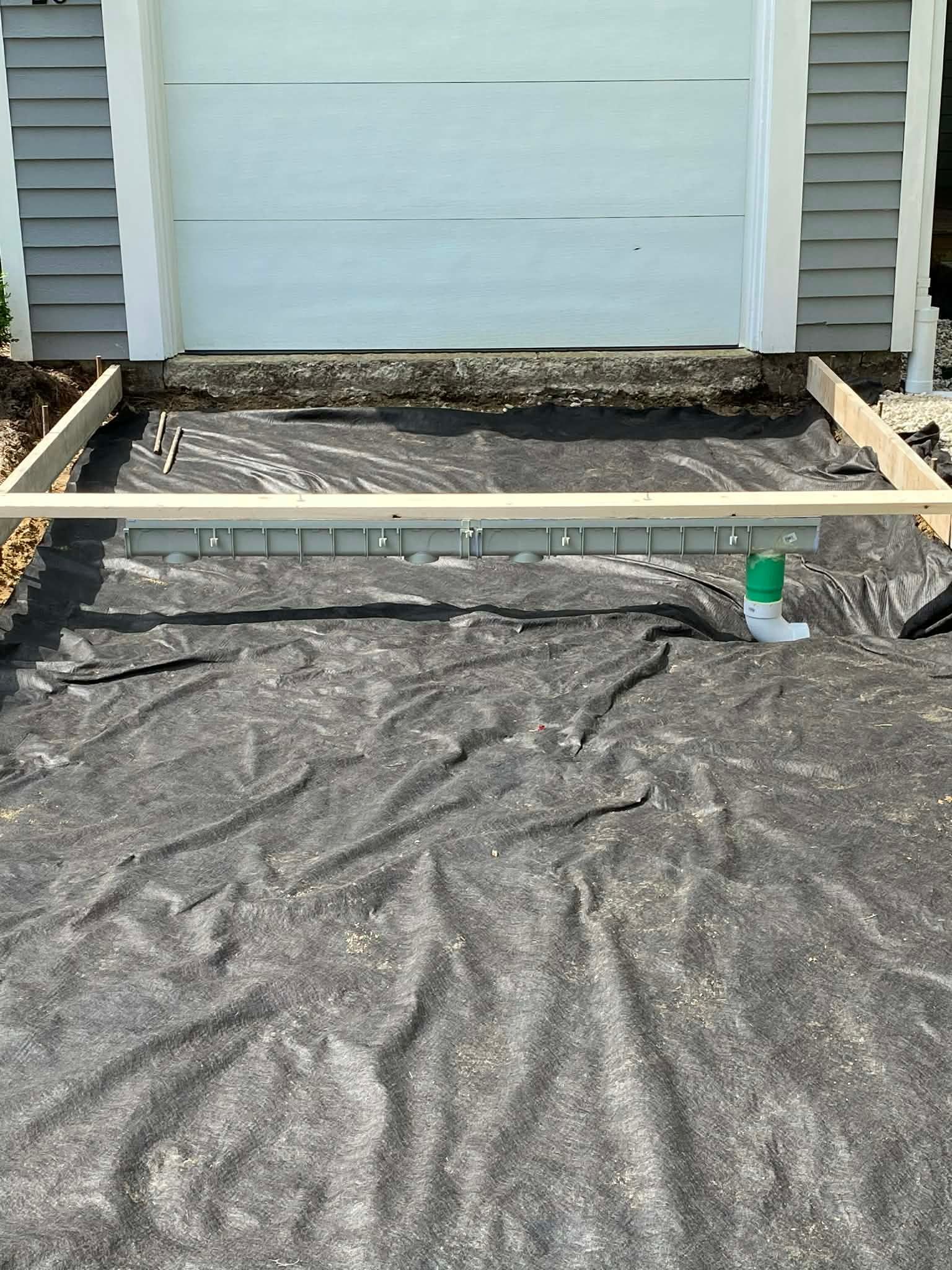 Construction site in front of a garage, with black fabric, wood frame, and drainage pipe.
