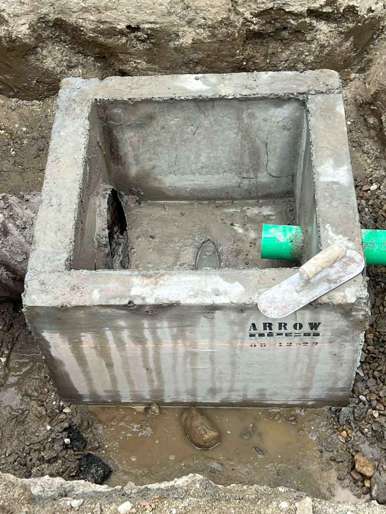 Concrete box in excavation, with green pipe and trowel. Construction site.