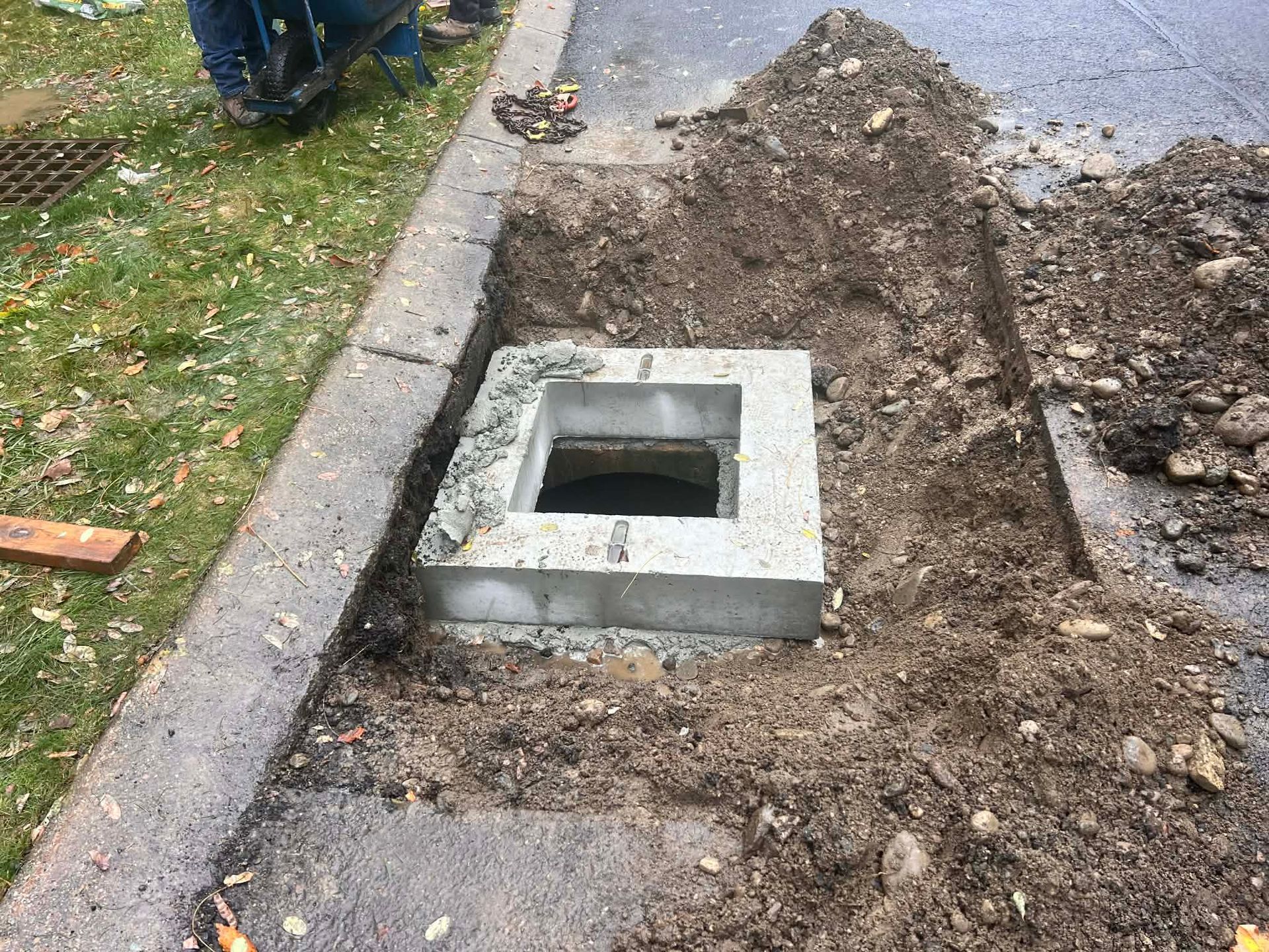 Excavated concrete drainage structure in asphalt. Dirt surrounds the curb.